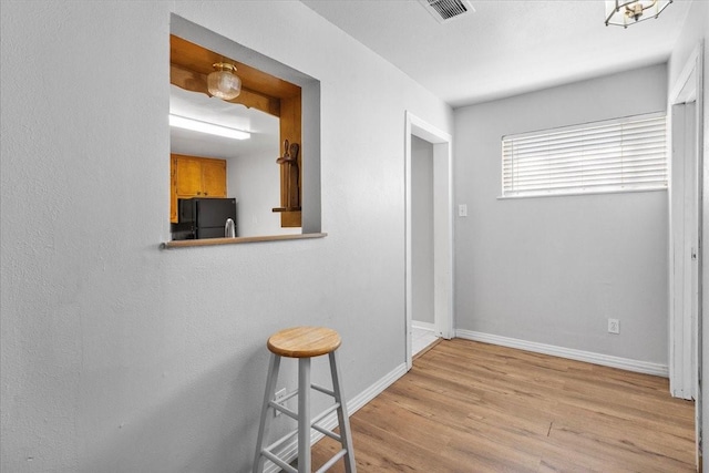 hall featuring light wood finished floors, visible vents, and baseboards