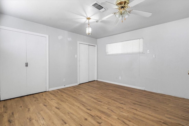 unfurnished bedroom with visible vents, baseboards, multiple closets, and wood finished floors