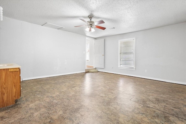 empty room with a textured ceiling, attic access, and baseboards