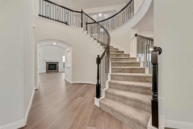 6926 Prairieside Trl, Prairie Ridge, TX 76084 - staircase featuring wood finished floors, baseboards, a high ceiling, a fireplace, and arched walkways
