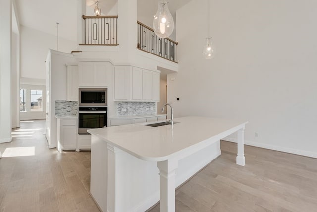kitchen with wall oven, a sink, light wood finished floors, built in microwave, and a towering ceiling