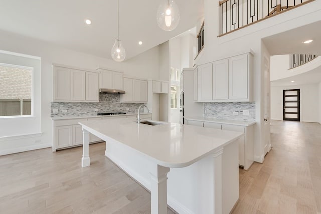 kitchen featuring a sink, backsplash, a high ceiling, a center island with sink, and light wood-type flooring