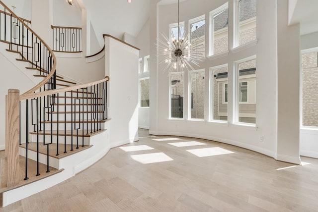 foyer entrance featuring a chandelier, wood finished floors, a towering ceiling, stairway, and baseboards