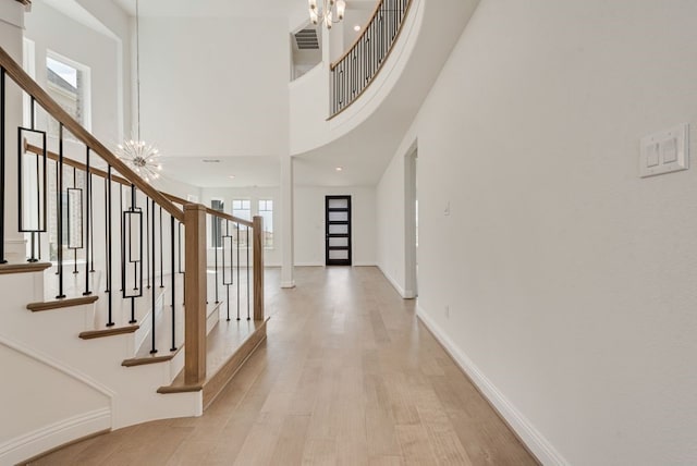 foyer with a chandelier, stairway, light wood finished floors, a towering ceiling, and baseboards