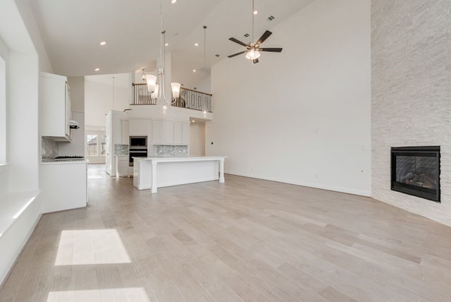 unfurnished living room featuring high vaulted ceiling, a fireplace, ceiling fan, light wood finished floors, and recessed lighting