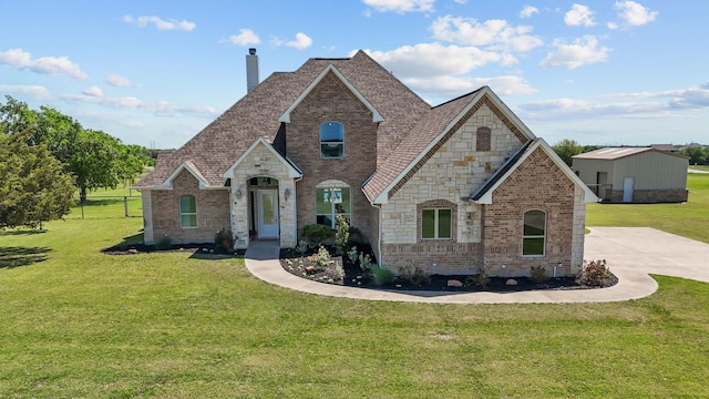 french provincial home featuring a chimney, brick siding, stone siding, and a front yard