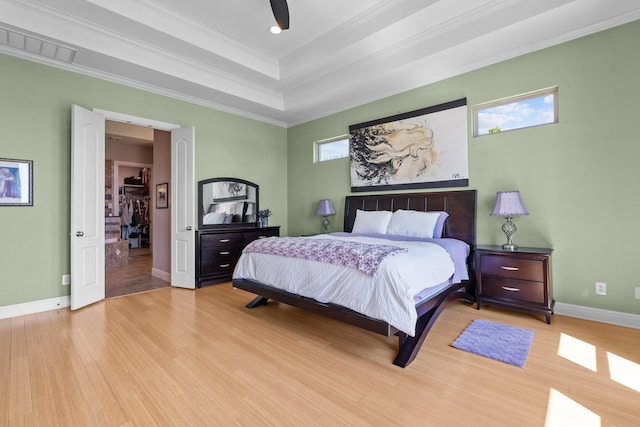 bedroom with crown molding, light wood-type flooring, a raised ceiling, baseboards, and visible vents
