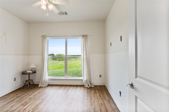 empty room with wainscoting, a ceiling fan, light wood-style floors, and visible vents