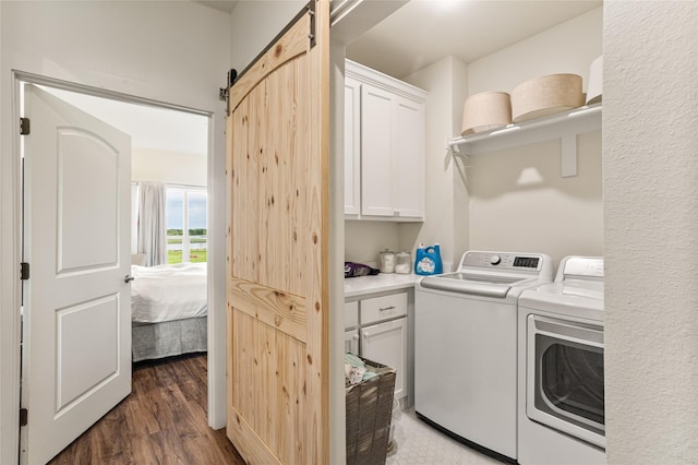 clothes washing area with cabinet space, a barn door, dark wood-style floors, and washer and clothes dryer