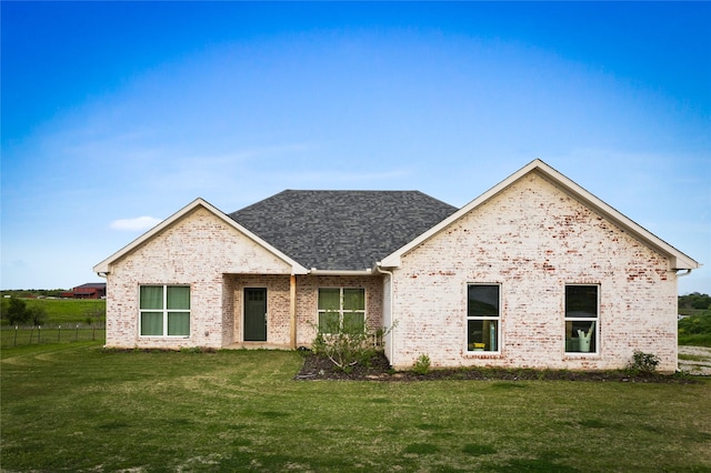 view of front facade featuring fence, a shingled roof, brick siding, and a front yard