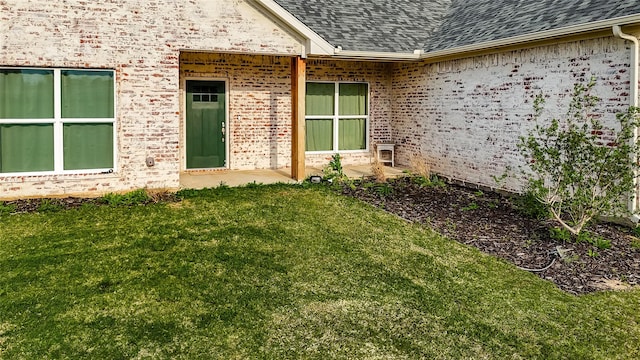property entrance with a lawn, brick siding, and a shingled roof