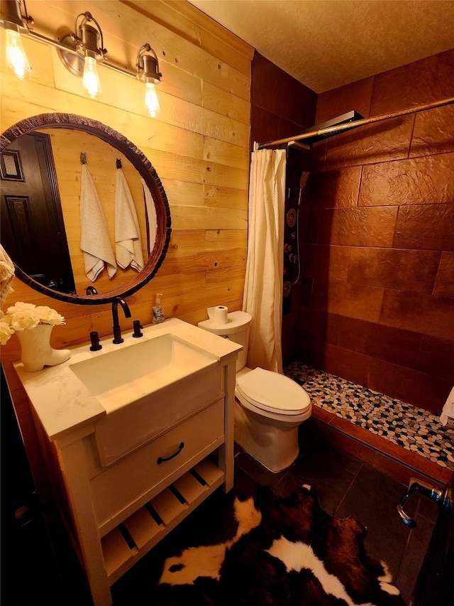 full bath with wooden walls, vanity, a tile shower, and toilet