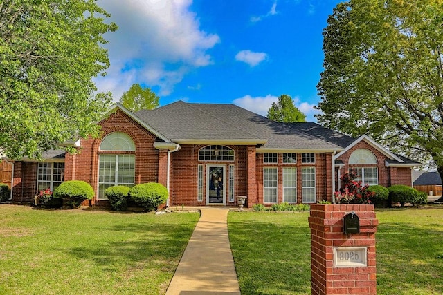ranch-style home with brick siding, a front yard, and a shingled roof