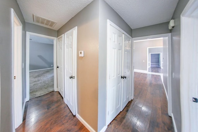 hall with a textured ceiling, baseboards, dark wood finished floors, and visible vents