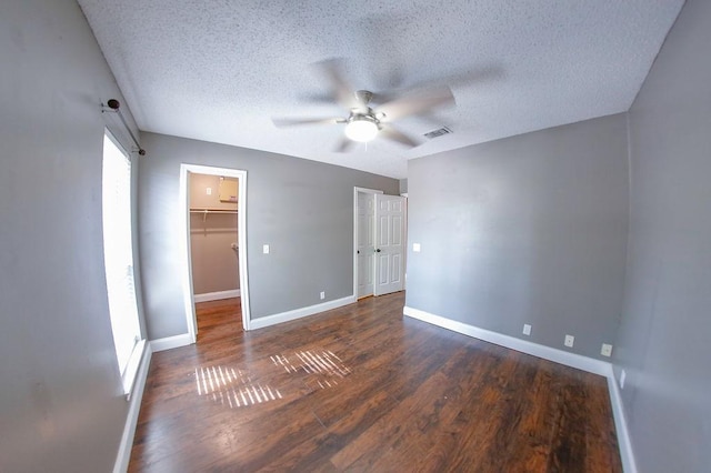 unfurnished bedroom featuring visible vents, baseboards, a spacious closet, a textured ceiling, and wood finished floors