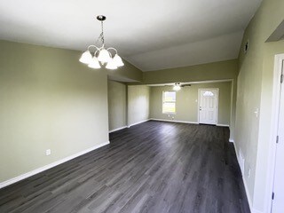 spare room with dark wood-style flooring, baseboards, and a notable chandelier