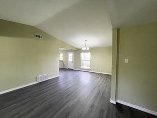 unfurnished living room with an inviting chandelier, vaulted ceiling, visible vents, dark wood-style flooring, and baseboards