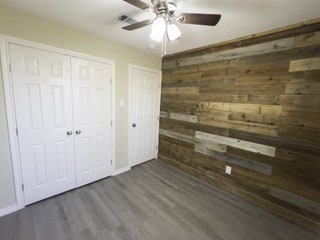 unfurnished bedroom featuring a closet, a ceiling fan, wood finished floors, wooden walls, and baseboards