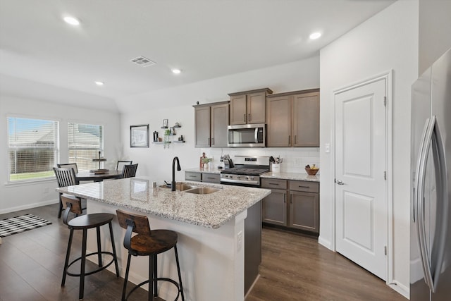 903 Saddle Club Way, Princeton, TX 75407 - kitchen with appliances with stainless steel finishes, dark wood finished floors, a kitchen island with sink, a breakfast bar area, and light stone counters