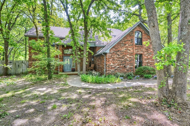 view of front of home featuring roof with shingles, fence, and brick siding
