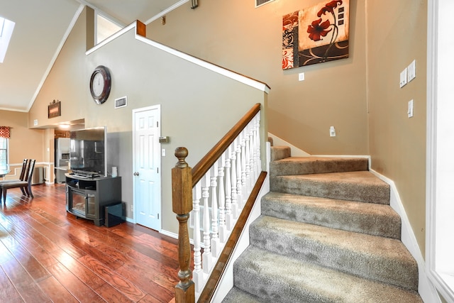 stairs featuring visible vents, baseboards, a skylight, high vaulted ceiling, and hardwood / wood-style floors