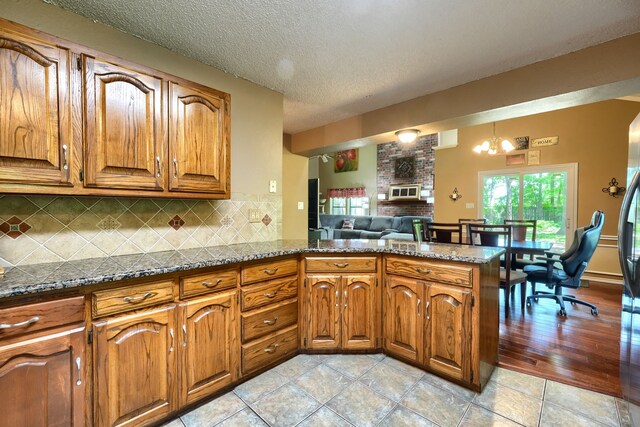 kitchen with a fireplace, a peninsula, a textured ceiling, backsplash, and brown cabinets