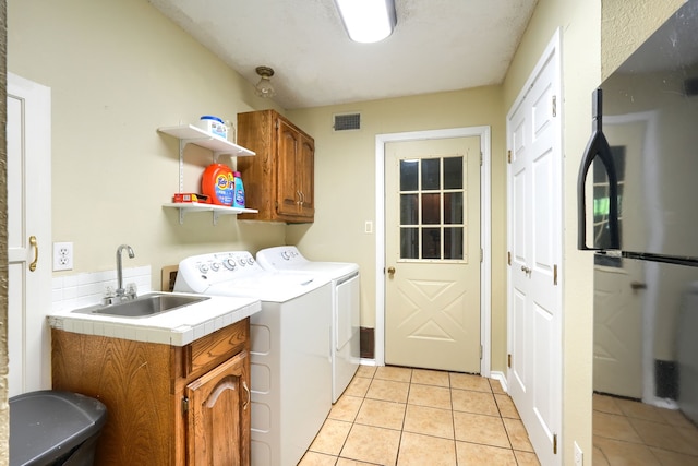 laundry area featuring visible vents, light tile patterned floors, a sink, cabinet space, and washing machine and dryer