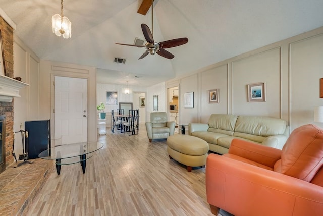living area featuring light wood-type flooring, vaulted ceiling, visible vents, a decorative wall, and ceiling fan with notable chandelier