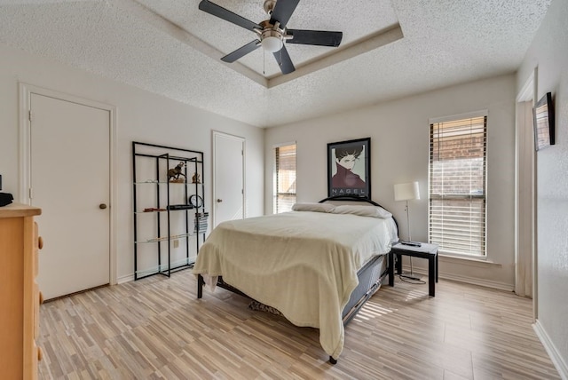 bedroom featuring light wood-style flooring, multiple windows, baseboards, and a textured ceiling