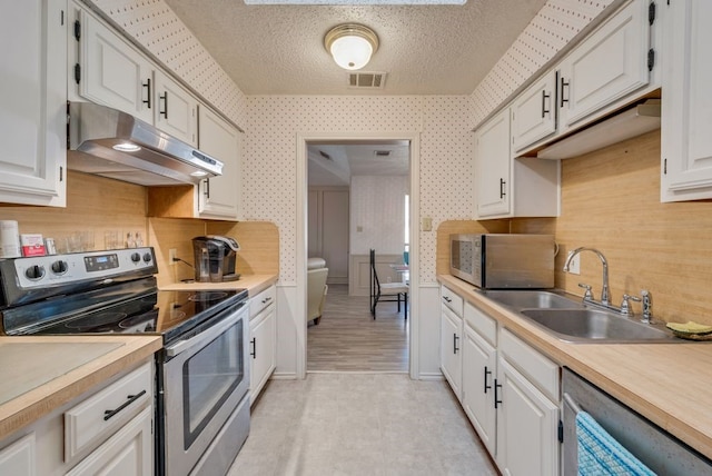 kitchen with visible vents, a sink, appliances with stainless steel finishes, under cabinet range hood, and wallpapered walls