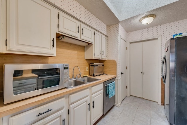 kitchen featuring a sink, wallpapered walls, light countertops, and stainless steel appliances