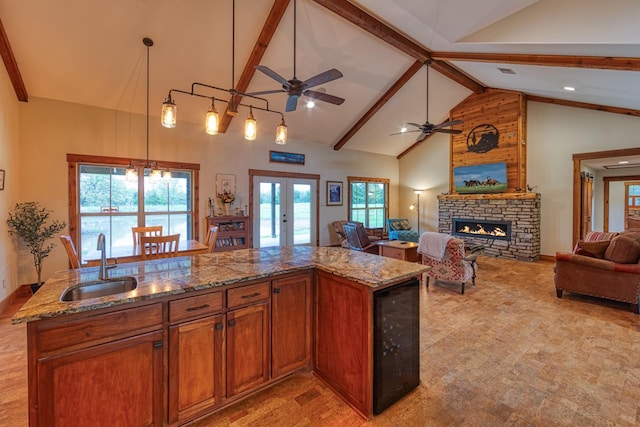 kitchen with a fireplace, light stone counters, a sink, beverage cooler, and open floor plan