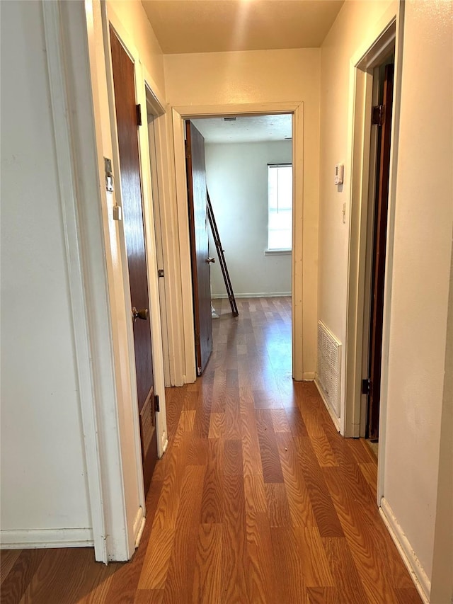 hallway with visible vents, baseboards, and wood finished floors