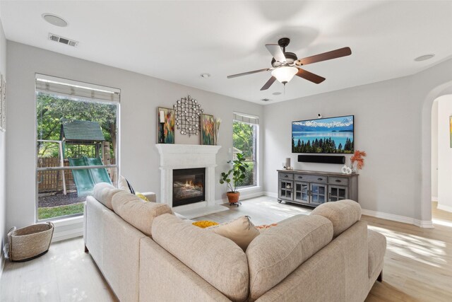 living area featuring visible vents, a glass covered fireplace, ceiling fan, light wood-type flooring, and arched walkways