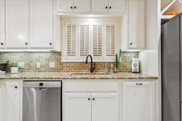 kitchen with white cabinets, a sink, appliances with stainless steel finishes, light stone countertops, and decorative backsplash