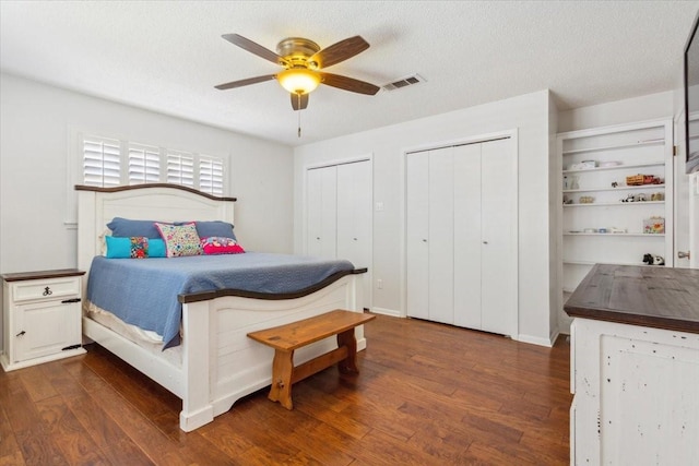 bedroom featuring ceiling fan, dark wood finished floors, a textured ceiling, visible vents, and multiple closets