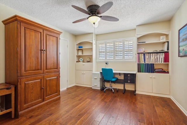 home office with dark wood-type flooring, a textured ceiling, built in features, and ceiling fan