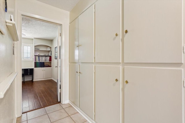 hallway with a textured ceiling and light tile patterned floors