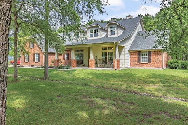 view of front of home featuring roof with shingles, a front yard, brick siding, and a chimney