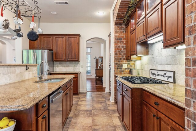 kitchen with arched walkways, light stone counters, a sink, stainless steel appliances, and decorative backsplash