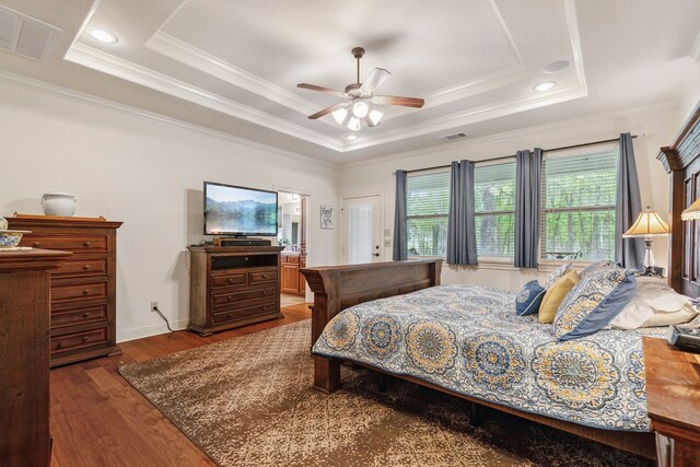 bedroom with ornamental molding, a tray ceiling, visible vents, and wood finished floors