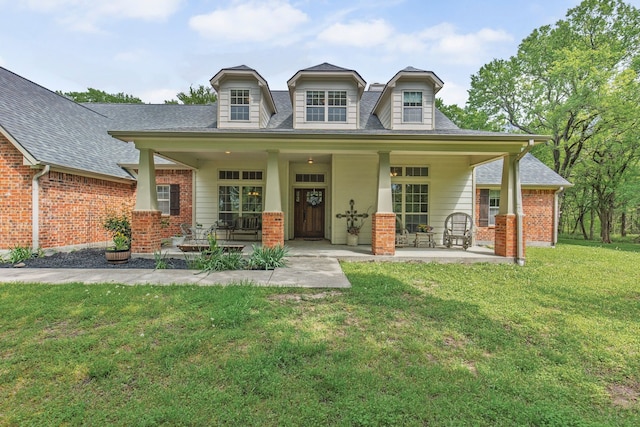 view of front of property featuring roof with shingles, covered porch, a front yard, and brick siding