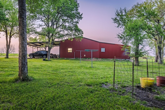 yard at dusk with a carport, fence, and an outbuilding