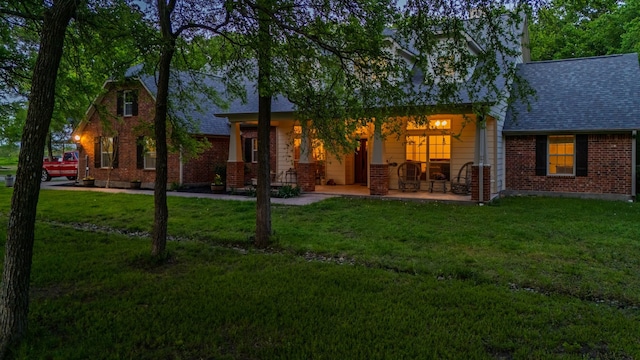 back of house with brick siding, a lawn, and roof with shingles