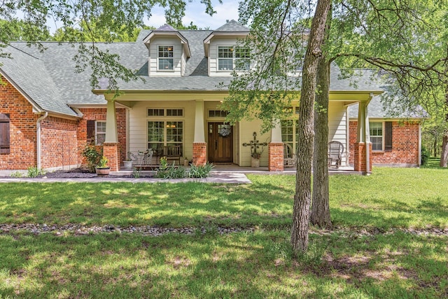 view of front facade featuring brick siding, a front yard, a porch, and roof with shingles