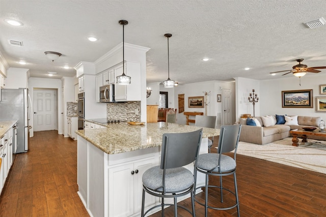 kitchen featuring dark wood-style flooring, open floor plan, visible vents, a breakfast bar area, and stainless steel appliances