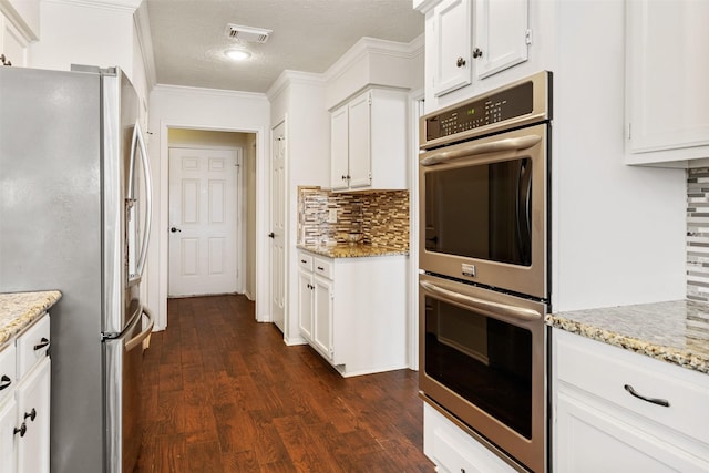 kitchen featuring dark wood-style flooring, backsplash, white cabinets, visible vents, and appliances with stainless steel finishes