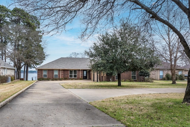 ranch-style house with concrete driveway, roof with shingles, brick siding, and a front lawn