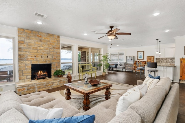 living room featuring visible vents, a ceiling fan, a textured ceiling, crown molding, and dark wood-type flooring