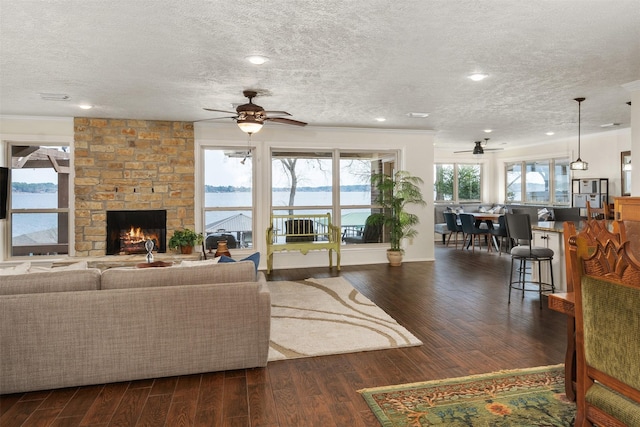 living room featuring dark wood-style flooring, ornamental molding, a fireplace, a textured ceiling, and ceiling fan